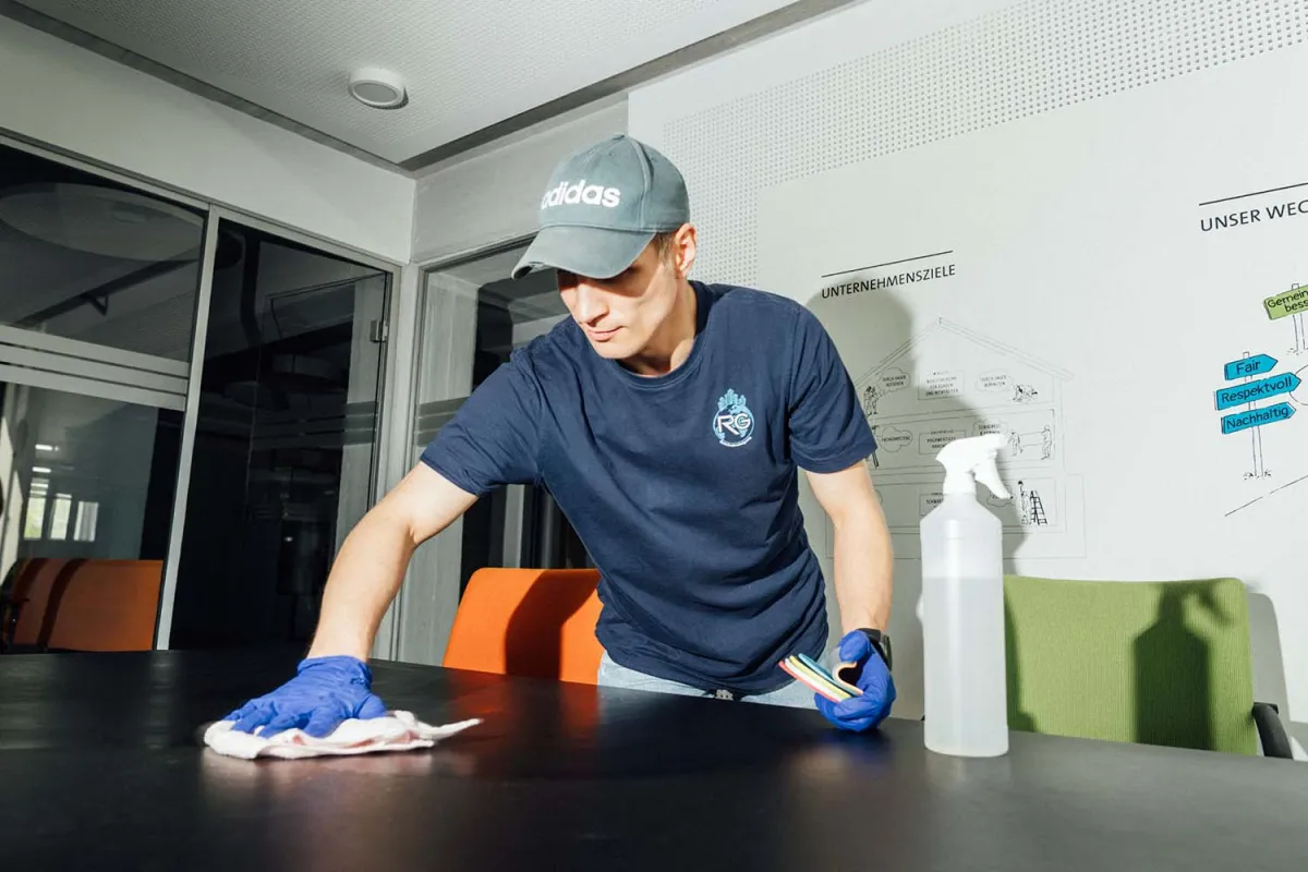 Mitarbeiter der RG Gebäudereinigung reinigt einen Tisch in einem Büroraum