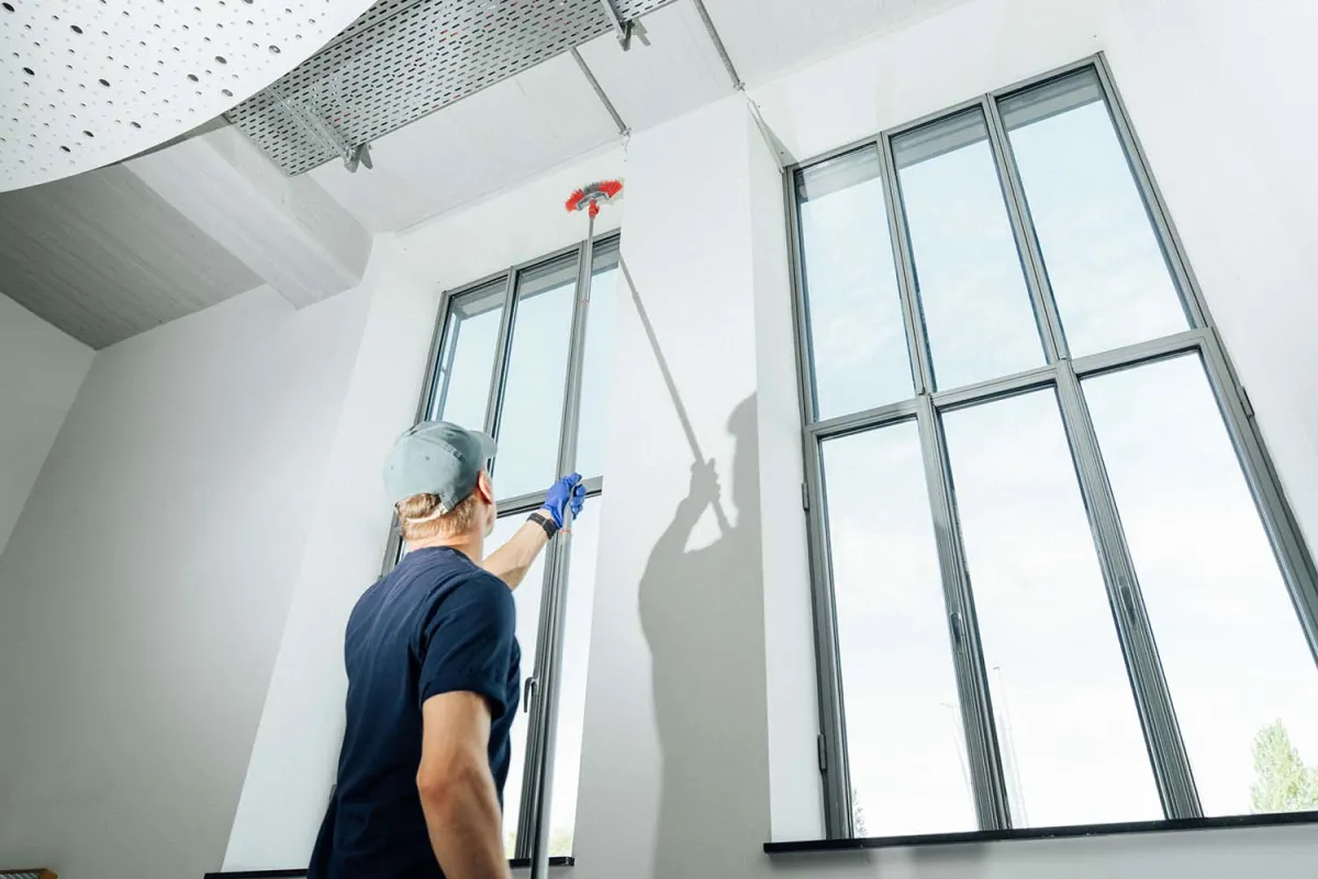 Mitarbeiter reinigt eine hohe Fensterfront im Innenraum
