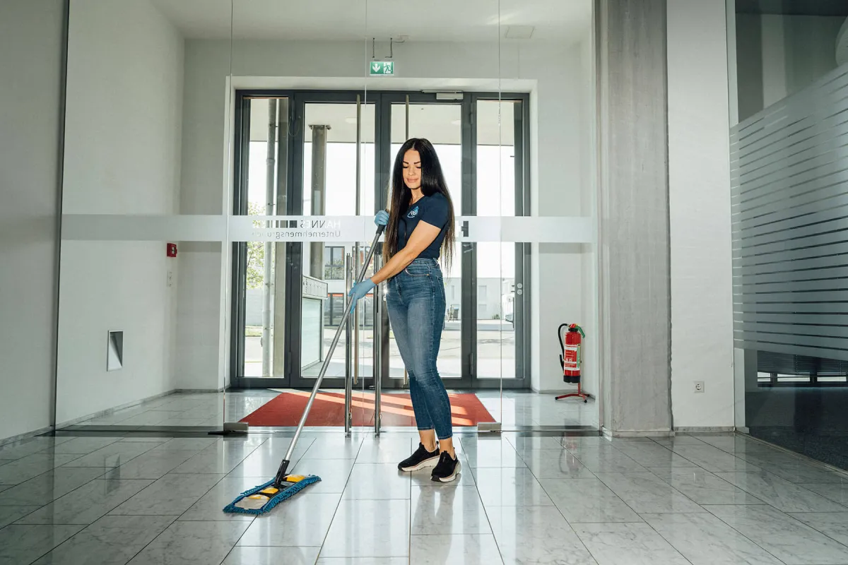 Reinigungskraft wischt den Boden im Eingangsbereich eines Gebäudes