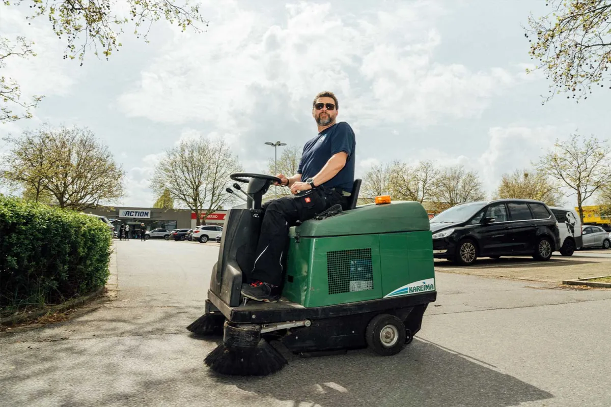 Mitarbeiter auf einer Aufsitzkehrmaschine reinigt einen Parkplatz